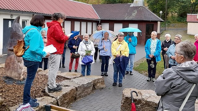 Eine Gruppe Frauen steht mit Regenschirmen und Jacken bei einem meditativen Abendspaziergang vor einem Fachwerkgebäude