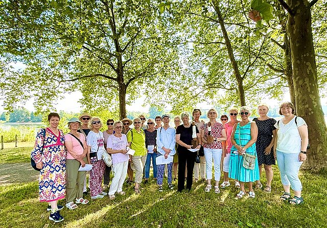 Gruppe von Frauen unterschiedlichen Alters steht im Schatten großer Bäume auf einer Wiese an einem sonnigen Tag