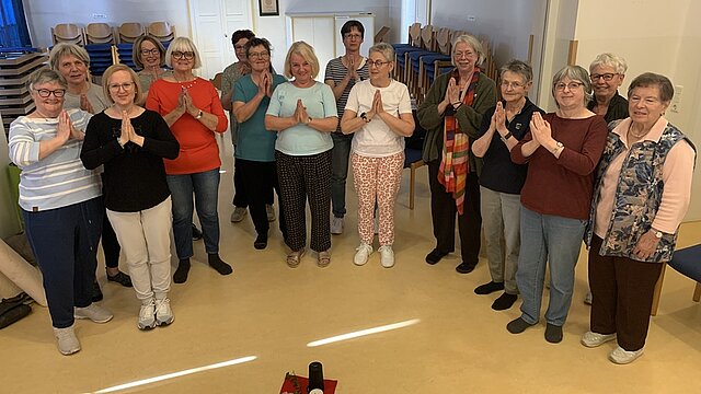 Eine Gruppe Frauen steht in einem Raum und hält die Hände vor der Brust in Gebetshaltung.